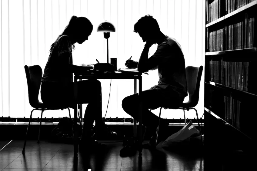 Silluette picture of two students sitting and studying in a library by a table 